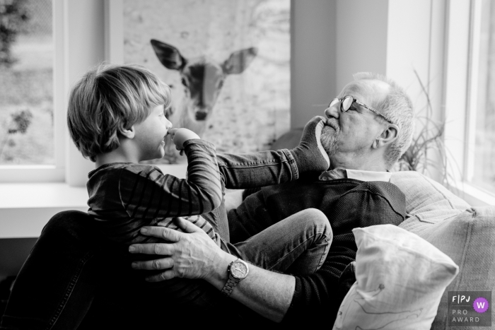 Un petit-fils pose le pied sur le visage de son grand-père alors qu'ils sont assis ensemble sur le canapé sur cette photo enregistrée par un photographe de famille de style documentaire primé à Gelderland, aux Pays-Bas.