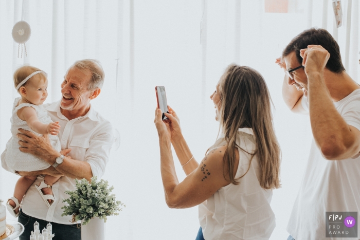 A grandfather holds his granddaughter as her mother takes a picture in this documentary-style family image recorded by a Florianopolis photographer. 