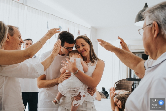 A mother and father hold their baby as family members extent their arms toward her in this Family Photojournalist Association contest awarded photo created by a Florianopolis family photographer. 