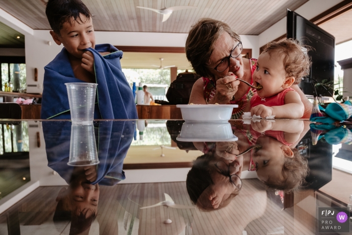 A grandmother feeds her granddaughter in this documentary-style family photo captured by a Florianopolis photographer. 