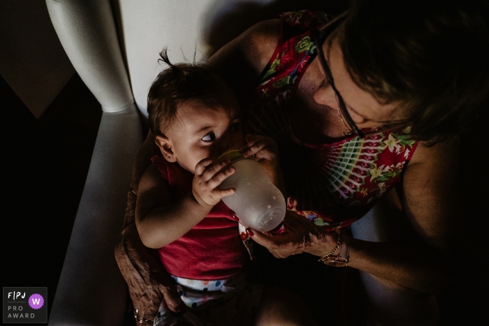 A grandmother feeds her granddaughter in this photograph by a Florianopolis documentary family photographer. 