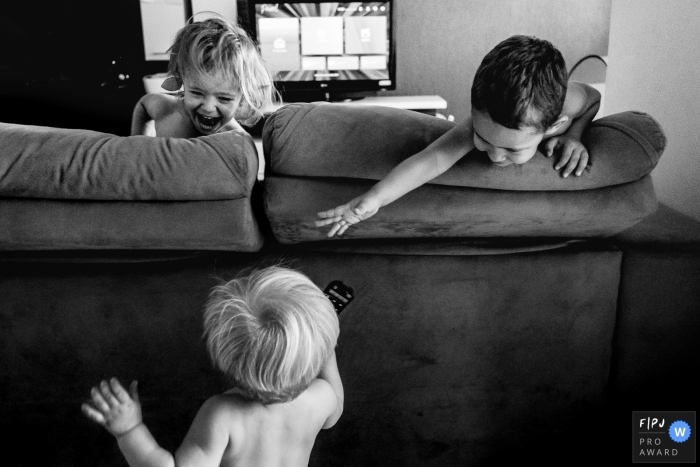 Un petit garçon tente de saisir la télécommande de son frère derrière le canapé sur cette photo prise par un photojournaliste de famille du Rio Grande do Sul, Brésil.