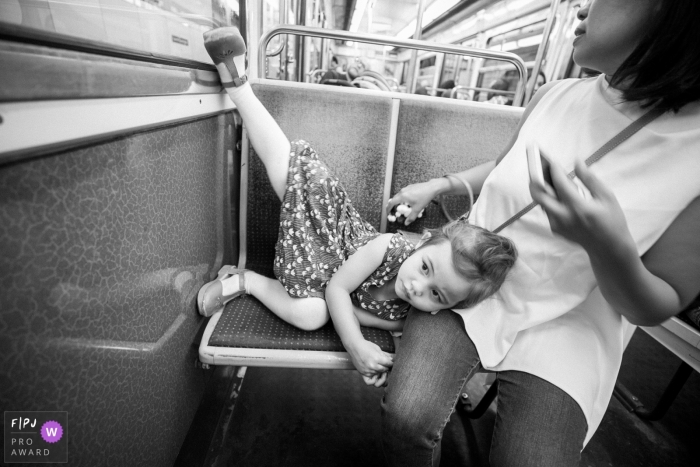 Photo by: <a href="https://www.fpja.com/documentary-family-photography-contests/faith-iskandar/paris/2094606">Faith Iskandar - France</a> A little girl lays on her mother's lap with her leg up on the wall as they ride on a subway in this photo by a Paris, France award-winning family photographer.