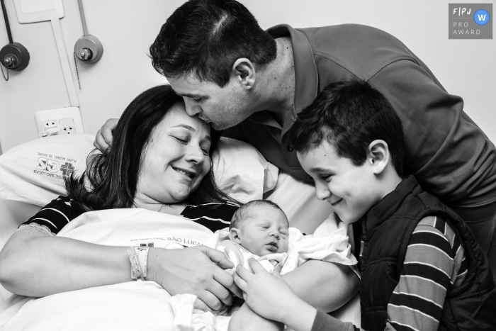 A husband visits his wife in the hospital with his son to meet their newborn baby in this black and white birth picture captured by a Rio de Janeiro, Brazil photographer.