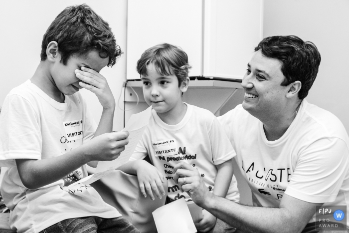 A father and brother sit with a little boy as he tears up reading a letter in this documentary-style family image recorded by a Rio de Janeiro, Brazil photographer. 