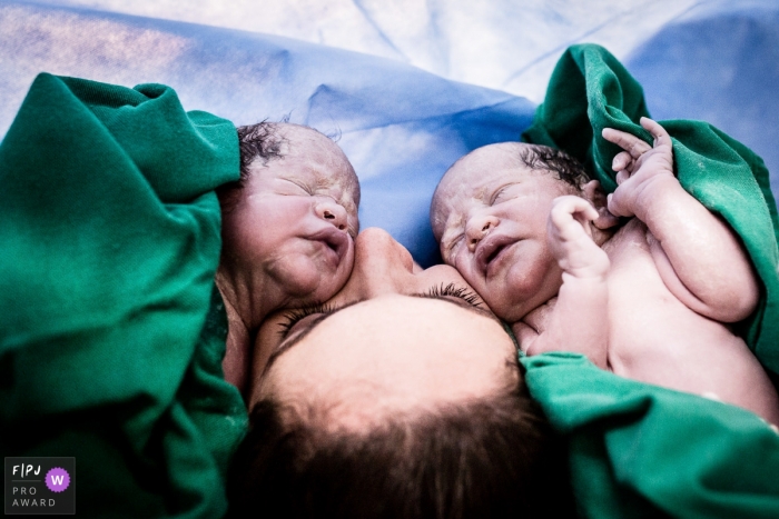 A mother hugs her newborn twins in the hospital in this photo by a documentary-style Rio de Janeiro birth photographer.