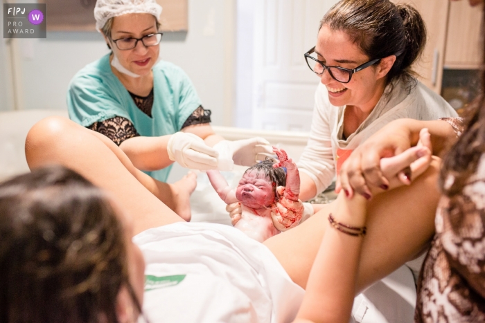 Photo by: <a href="https://www.fpja.com/documentary-family-photography-contests/ana-paula-amado/maca%C3%A9/2095056">Ana Paula Amado - Brazil</a> A nurse holds a woman's newborn baby immediately after birth in this award-winning photo captured by a Rio de Janeiro birth photographer.