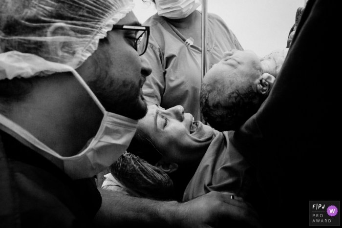 Photo by: <a href="https://www.fpja.com/documentary-family-photography-contests/ana-paula-amado/maca%C3%A9/2095111">Ana Paula Amado - Brazil</a> A husband supports his wife as the two of them get to see their infant for the first time in the hospital in this black and white birth photo by a Rio de Janeiro photographer.