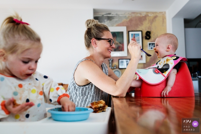 A baby smiles and laughs as his mother feeds him in this family picture by a Kent, England photographer. 