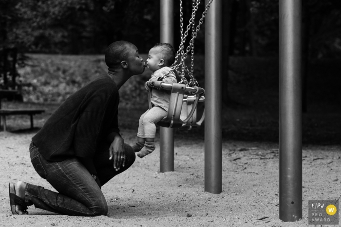 Photo by: <a href="https://www.fpja.com/documentary-family-photography-contests/liesbeth-parlevliet/zuid-holland/2095386">Liesbeth Parlevliet - Netherlands</a> A mother kisses her daughter as she sits in a swing in this FPJA award-winning image captured by a Netherlands family photographer.