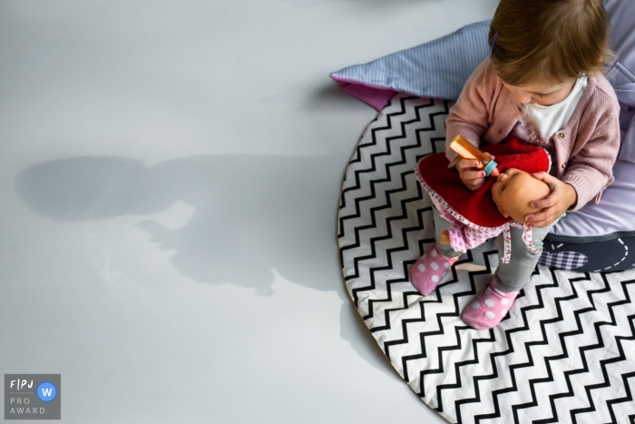 Photo by: <a href="https://www.fpja.com/documentary-family-photography-contests/nathalie-moors/antwerpen/2096091">Nathalie Moors - Belgium</a> A little girl feeds her baby doll in this family picture by an Antwerpen photographer.