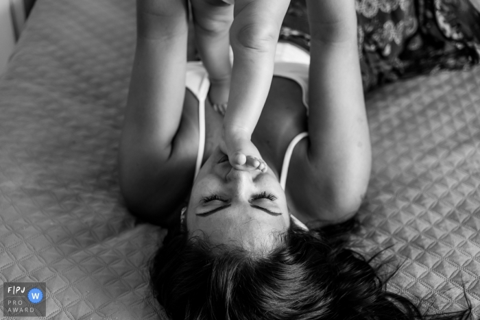 Photo by: <a href="https://www.fpja.com/documentary-family-photography-contests/liliane-cotta/rio-de-janeiro/2096216">Liliane Cotta - Brazil</a> A baby stands on top of mom who lays on a bed in this photograph by a Rio de Janeiro, Brazil documentary family photographer.