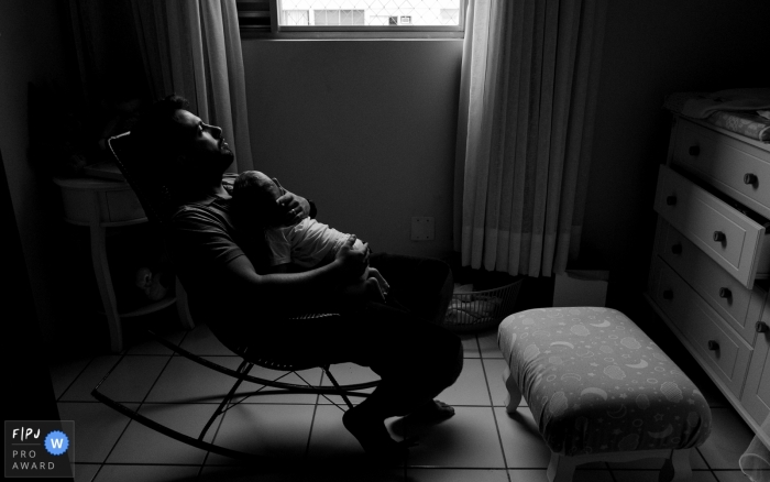 Photo by: <a href="https://www.fpja.com/documentary-family-photography-contests/lisandro-castro/cuiab%C3%A1/2096316">Lisandro Castro - Brazil</a> A father holds his infant as he sits in a rocking chair in this award-winning photo by a Cuiaba family photographer.