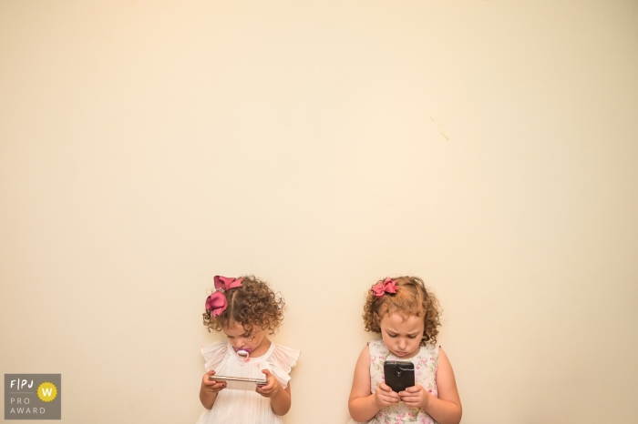 Two girls stand next to each other looking at phones in this photograph created by a Campinas family photojournalist. 