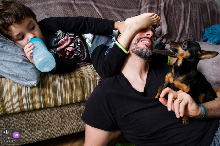 A little boy puts his foot on his father's face while he holds their small dog in this photograph by a Sao Paulo, Brazil documentary family photographer. 