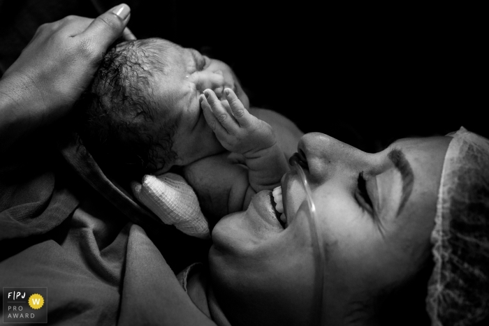 A mother smiles as she holds her baby in the hospital after giving birth in this photo captured by a Minas Gerais birth photographer.