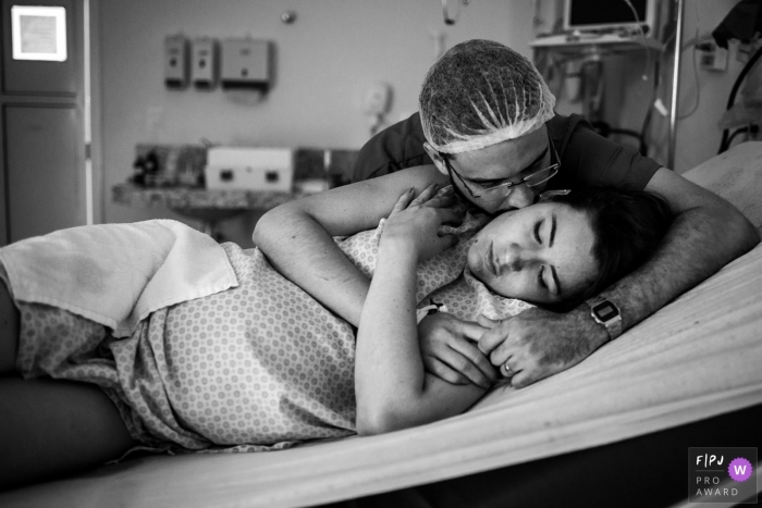 A husband lovingly holds his pregnant wife in this black and white photo captured during a hospital birthing session by a Brazil documentary family photographer 