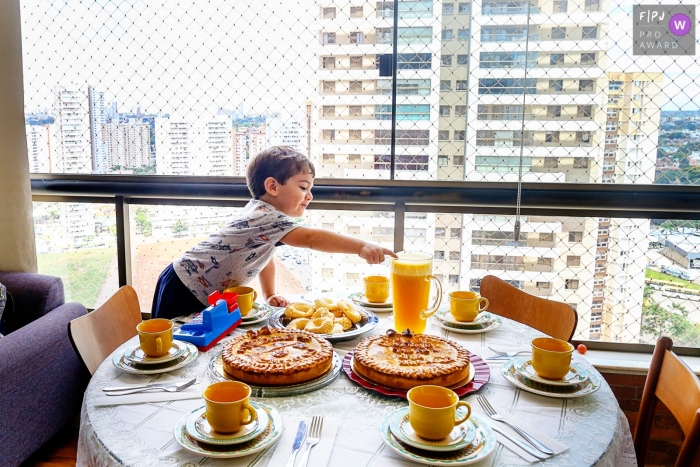 Photo by: <a href="https://www.fpja.com/documentary-family-photography-contests/claudia-amorim/goiania/2097616">Claudia Amorim - Brazil</a> A little boy reaches across a table for the pitcher of orange juice in this award-winning photo by a Goiania family photographer.