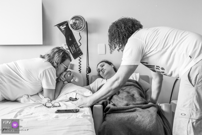 A woman and husband support a pregnant woman in the hospital as she prepares to give birth in this photo captured by an award-winning Rio de Janeiro, Brazil birth photographer.