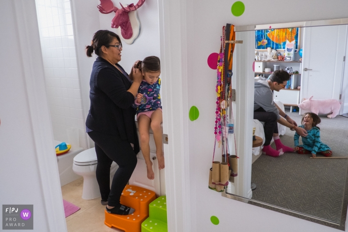 Une mère coiffe sa fille pendant que son mari réconforte leur autre fille qui pleure sur cette photographie créée par un photojournaliste de la famille de Los Angeles, en Californie.