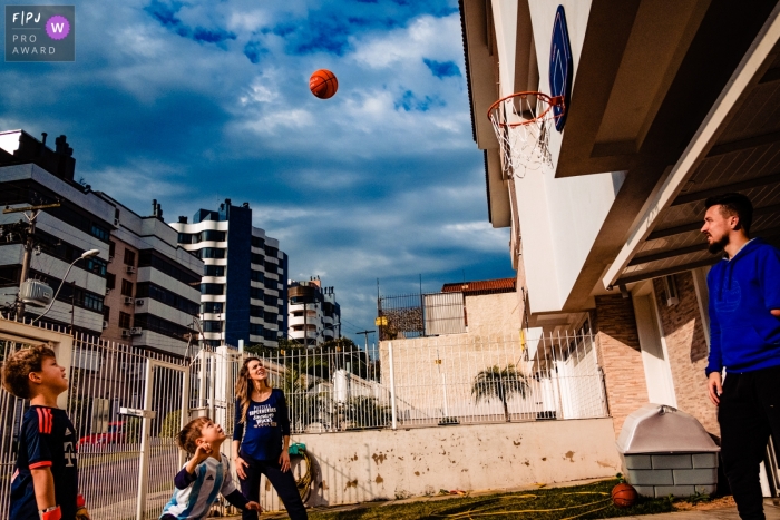 Une famille joue au basket ensemble devant leur maison dans cette image familiale de style documentaire, enregistrée par un photographe de Rio Grande do Sul, Brésil.