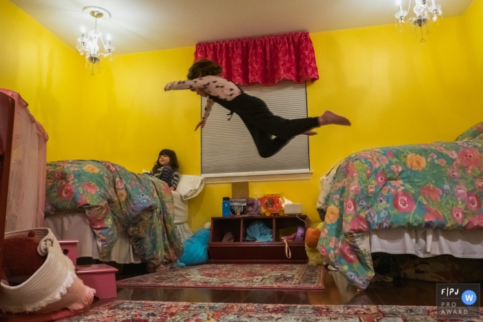Photo by: <a href="https://www.fpja.com/documentary-family-photography-contests/annie-bang/los-angeles/2098296">Annie Bang - United States</a> A girl leaps from her bed onto her sister's in this award-winning photo by a Los Angeles, CA family photographer.