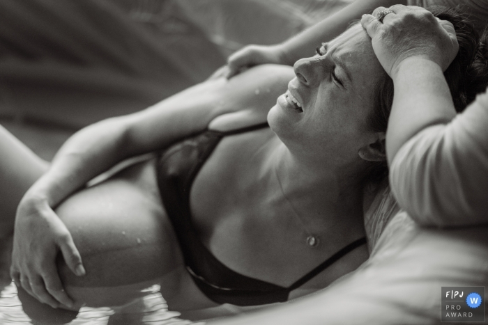 Photo by: <a href="https://www.fpja.com/documentary-family-photography-contests/meg-brock/philadelphia/2098431">Meg Brock - United States</a> A woman holds her stomach as she gives birth in her birthing tub in this award-winning image captured by a Philadelphia birth photographer.