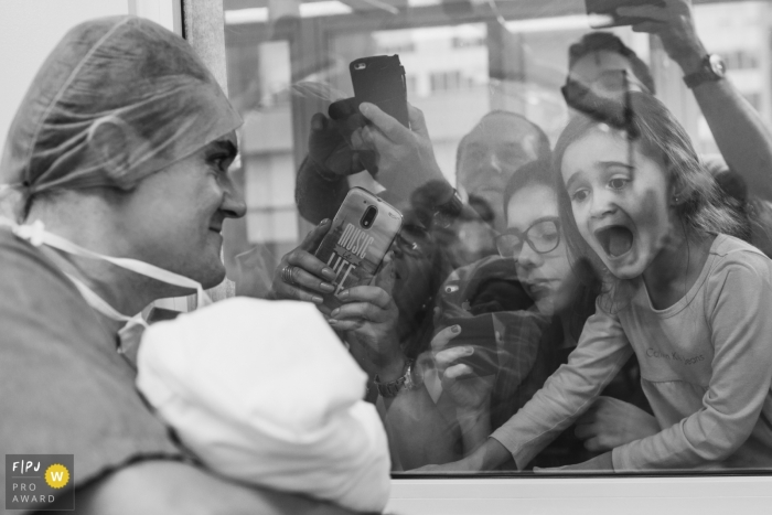 A family excitedly takes pictures through the hospital window as a nurse holds up their newest family member in this photo by a Sao Paulo, Brazil documentary birth photographer.