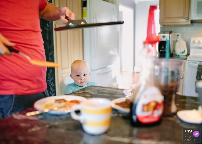 A baby boy watches as his father gets breakfast ready in this photograph created by a Philadelphia family photojournalist. 