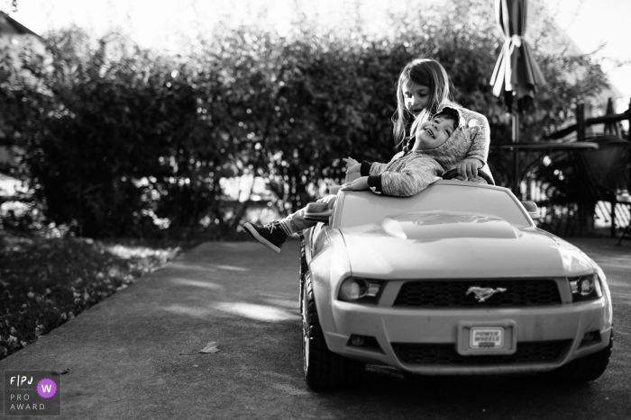 Un garçon et une fille jouent dans une petite voiture dans cette image de famille de style documentaire enregistrée par un photographe de Philadelphie.