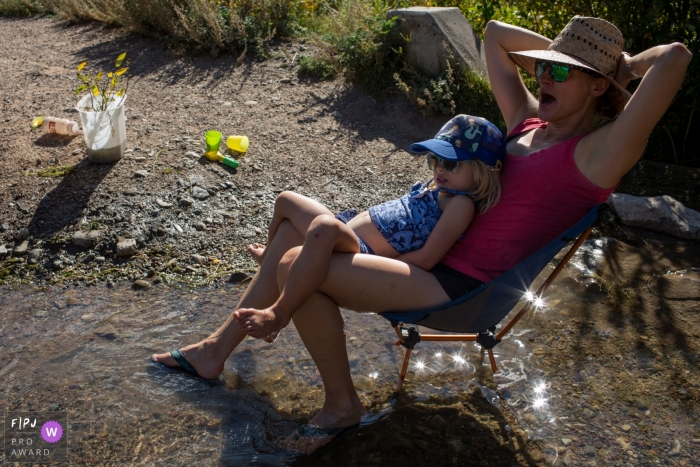 Photo by: <a href="https://www.fpja.com/documentary-family-photography-contests/casie-zalud/boulder/2098751">Casie Zalud - United States</a> A little girl sits on her mother's lap as they sit in a small stream in this FPJA award-winning picture by a Boulder, CO family photographer.