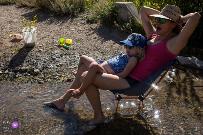 Une petite fille est assise sur les genoux de sa mère alors qu'ils sont assis dans un petit ruisseau sur cette photo primée FPJA par un photographe de la famille Boulder, CO.