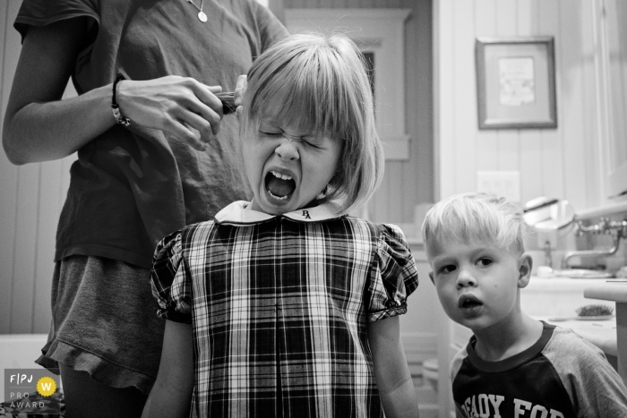 Une fille crie pendant que sa mère coiffe ses cheveux sur cette photo enregistrée par un photographe de famille de style documentaire primé à Key West, FL.