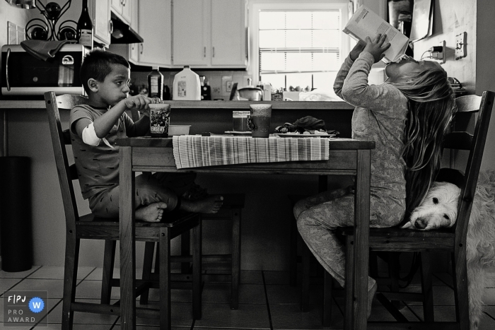 Photo by: <a href="https://www.fpja.com/documentary-family-photography-contests/julie-ambos/key-west/2099061">Julie Ambos - United States</a> A boy and girl eat breakfast together as their dog licks the girl's seat for crumbs in this picture captured by a Key West, FL family photojournalist.
