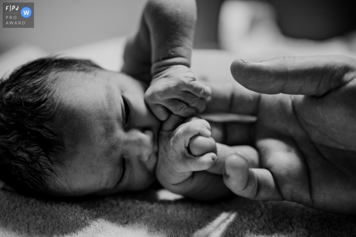 Photo by: <a href="https://www.fpja.com/documentary-family-photography-contests/karen-velleman/groningen/2099417">Karen Velleman - Netherlands</a> Netherlands dads hands with baby - Black and white newborn photography for Groningen