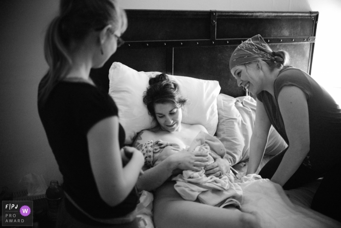 Photo by: <a href="https://www.fpja.com/documentary-family-photography-contests/samantha-moore/sarasota/2099428">Samantha Moore - United States</a> Surrounded by her midwives late in the night, a new mom holds her baby | FL Birth Photography