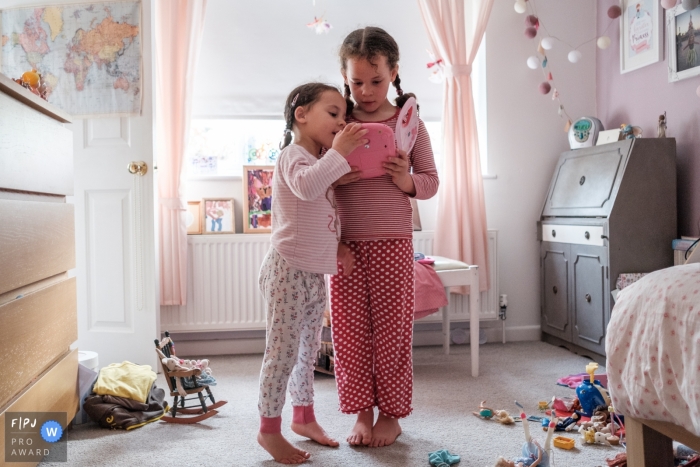 Photo by: <a href="https://www.fpja.com/documentary-family-photography-contests/jennifer-adams/gloucestershire/2099611">Jennifer Adams - United Kingdom</a> Gloucestershire family photography | Sisters huddle around a mobile device in their bedroom.
