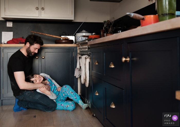 Photographe de famille britannique | Fille câlin avec son père sur le sol de la cuisine