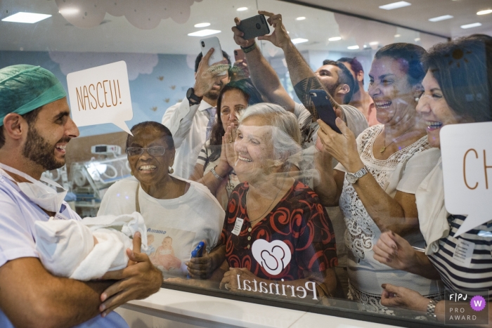 Photo by: <a href="https://www.fpja.com/documentary-family-photography-contests/clara-sampaio/rio-de-janeiro/2099648">Clara Sampaio - Brazil</a> Rio de Janeiro birth photos | Proud daddy showing off baby to hospital visitors in Brazil