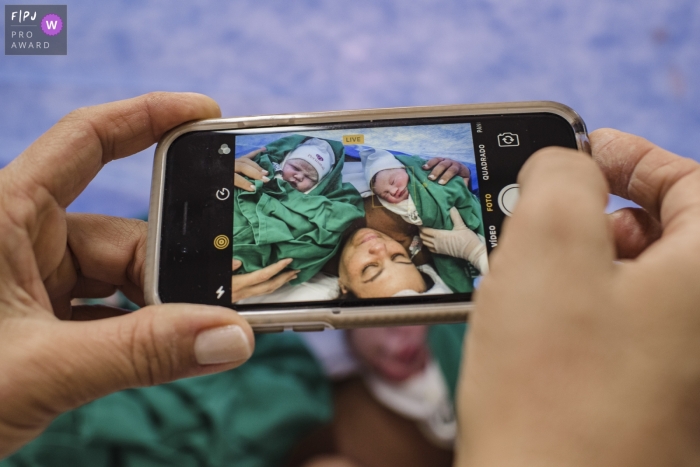 Photo by: <a href="https://www.fpja.com/documentary-family-photography-contests/clara-sampaio/rio-de-janeiro/2099652">Clara Sampaio - Brazil</a> Brazil detail photo of dad's phone screen showing mom with twin babies after delivering in Rio de Janeiro hospital.