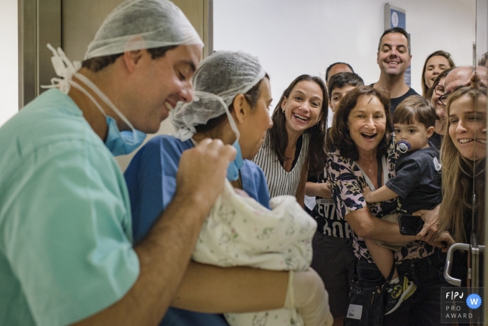 Photo by: <a href="https://www.fpja.com/documentary-family-photography-contests/clara-sampaio/rio-de-janeiro/2099656">Clara Sampaio - Brazil</a> Brazil birth photographer captured image of dad showing off new baby to his family in Rio de Janeiro