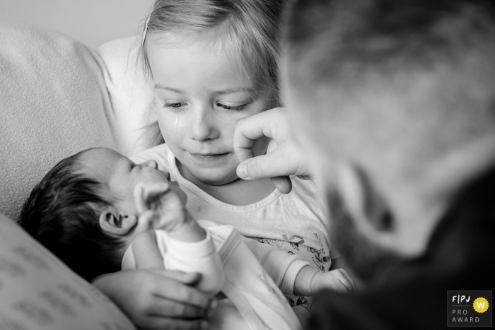 Nantes Family and Birth Photographer | Emotion of a girl holding her little baby sister as dad wipes her tears.