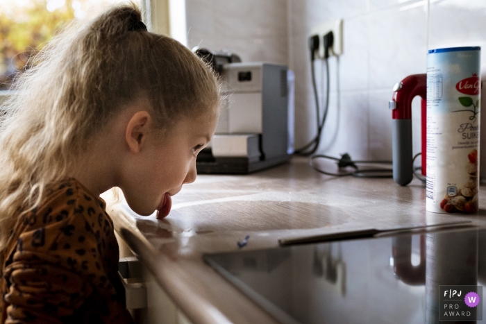 Photo by: <a href="https://www.fpja.com/documentary-family-photography-contests/gonda-meurs/noord-holland/2099862">Gonda Meurs - Netherlands</a> Noord Holland, Netherlands documentary-style photo of young girl licking sugar off the kitchen counter.