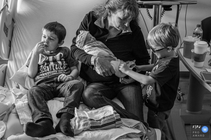 Photographie de naissance dans le Connecticut - Les enfants seront des enfants. Un grand frère vérifie les pieds de sa petite sœur, tandis que l'autre se cueille le nez sur le lit d'hôpital.