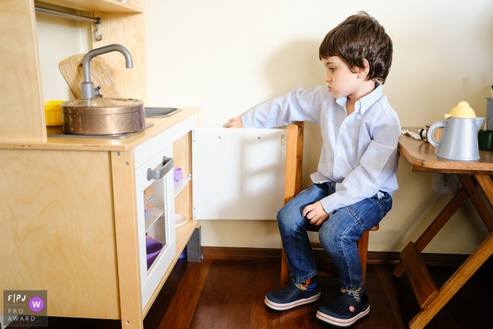 Photo by: <a href="https://www.fpja.com/documentary-family-photography-contests/nana-bonorino/rio-grande-do-sul/2100274">Nana Bonorino - Brazil</a> Rio Grande do Sul Family Photography | Boy playing kitchen, looking bored at the cupboard as if thinking, what am I going to cook?