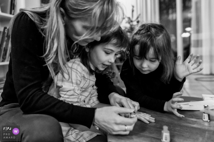 Photographe de famille france | La mère passe du temps avec ses filles pendant qu'elles appliquent du vernis à ongles.