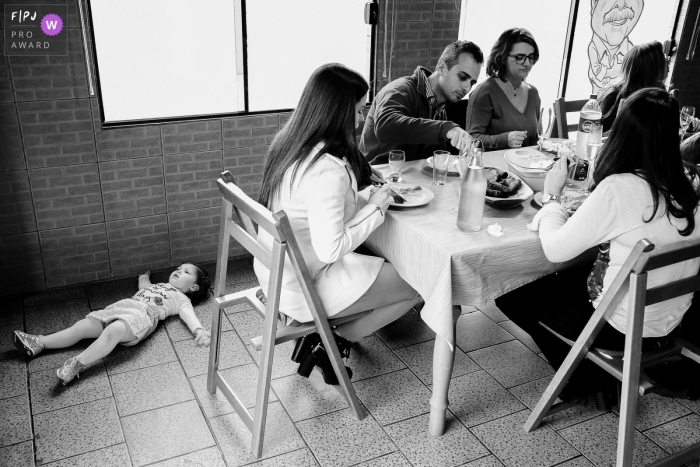 Rio Grande do Sul Family photography of a child lying on the floor as the family has lunch at the table.