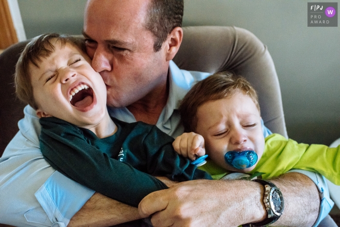 Photo by: <a href="https://www.fpja.com/documentary-family-photography-contests/claudia-ruiz/rio-de-janeiro/2100557">Claudia Ruiz - Brazil</a> Rio de Janeiro Family Photograph of a father sitting with and kissing his crying children