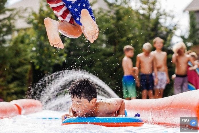 Photo by: <a href="https://www.fpja.com/documentary-family-photography-contests/ron-storer/seattle/2100793">Ron Storer - United States</a> Kids play in the water on a slip and slide in Seattle - Washington family photography