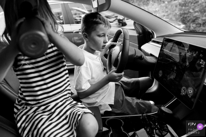 Photo: <a href="https://www.fpja.com/documentary-family-photography-contests/ron-storer/seattle/2100799"> Ron Storer - États-Unis </a> Enfants de Seattle jouant au volant d'un jeu vidéo sur un photographe de famille Tesla - WA